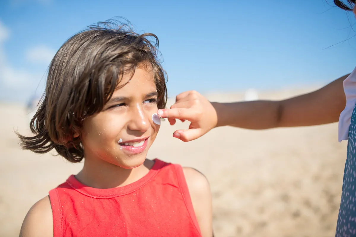 Una niña en la playa mientras le ponen protector solar en la cara