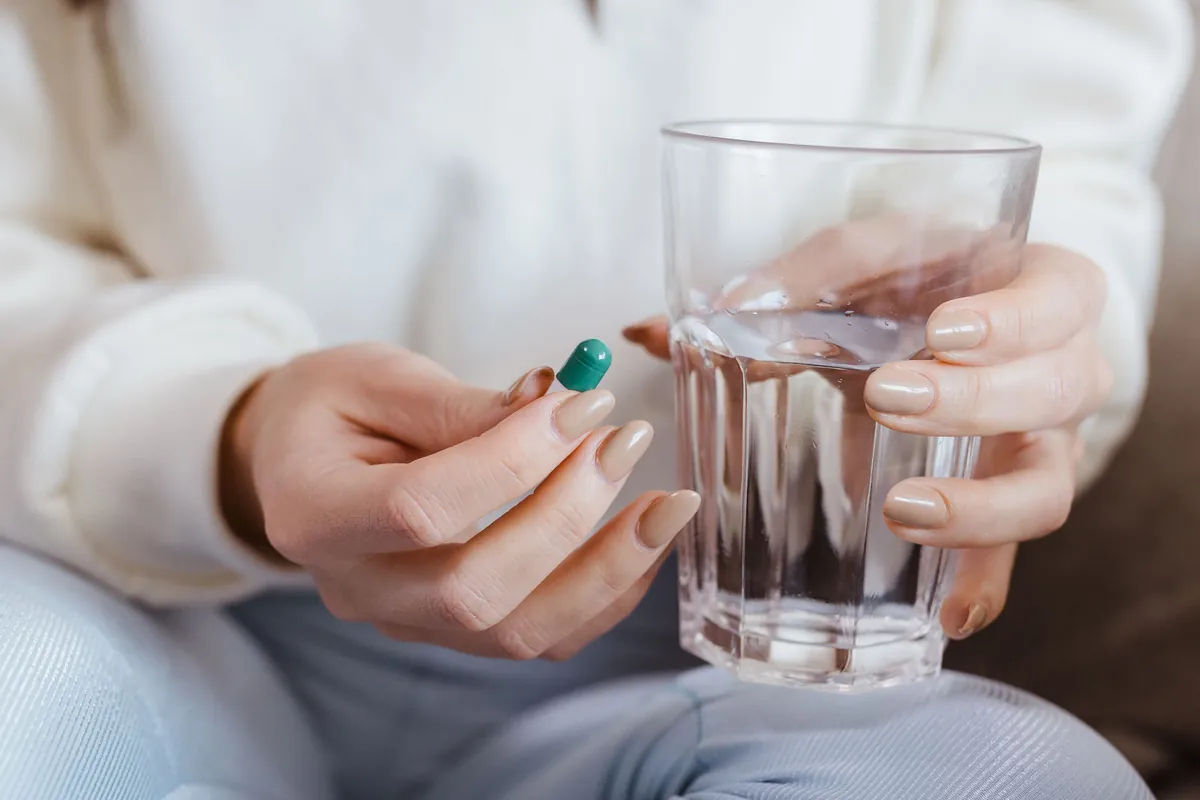 Mujer con una cápsula en la mano y un vaso de agua